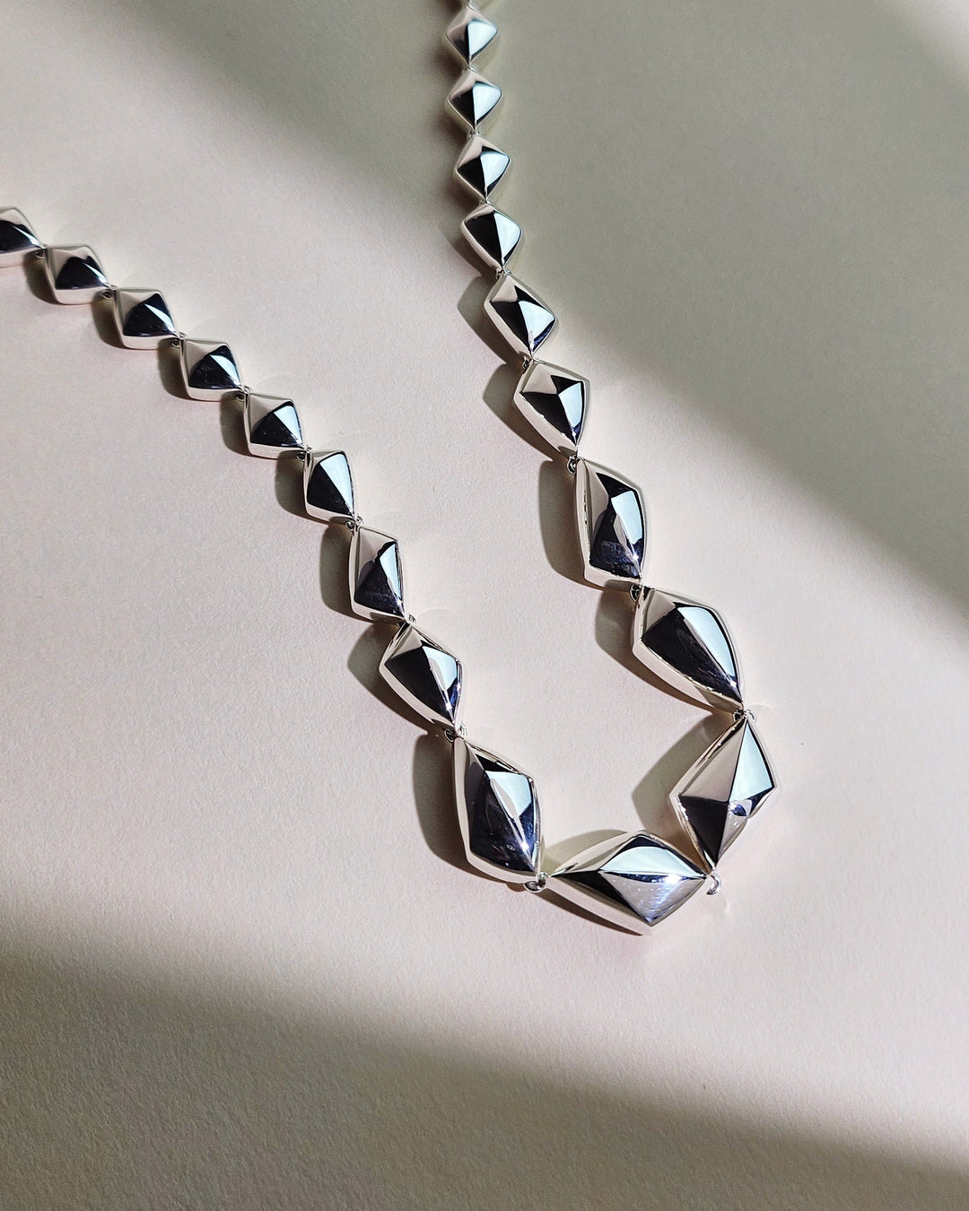 Sculptural silver necklace with geometric links arranged in a continuous form.