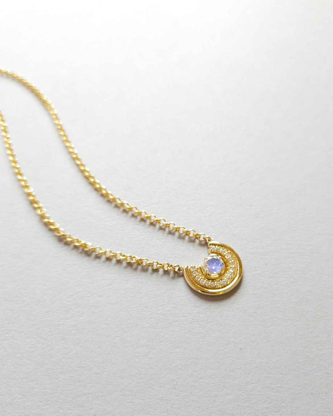14K Gold necklace with an arc pendant featuring rainbow moonstone and diamonds on a light gray background
